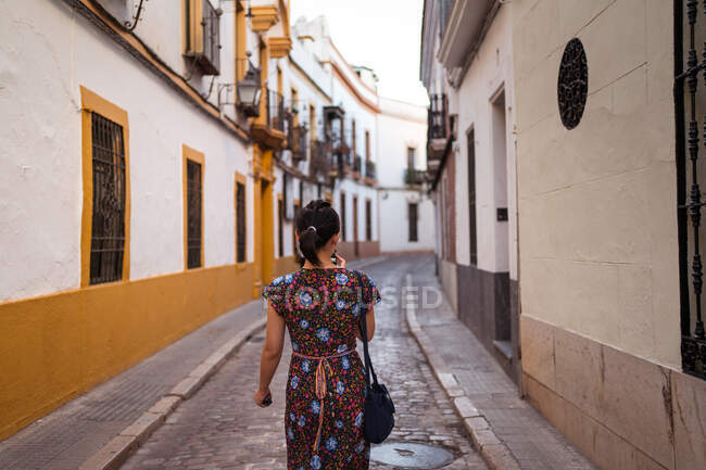 Atrás vista de anónimo asiático mujer turista de pie en estrecho pasaje entre casas en la ciudad - foto de stock