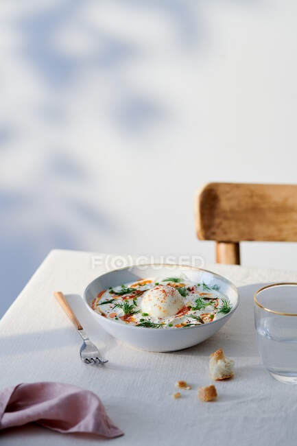 Высокий угол керамической миски с турецкими яйцами на столе возле стакана воды и вилки — стоковое фото