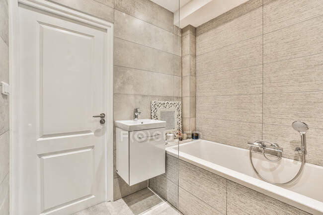 Bagno moderno interno con vasca e parete piastrellata grigia contro lavabo in casa luce — Foto stock