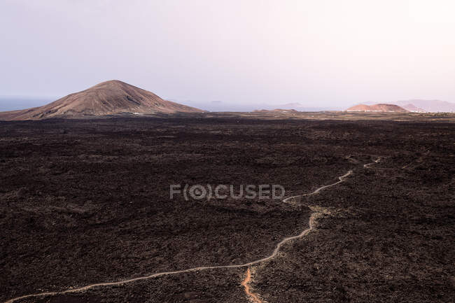 Desde arriba ruta áspera entre lava oscura contra los volcanes Caldera Blanca y Caldereta en el Parque Natural de Lanzarote Islas Canarias España - foto de stock
