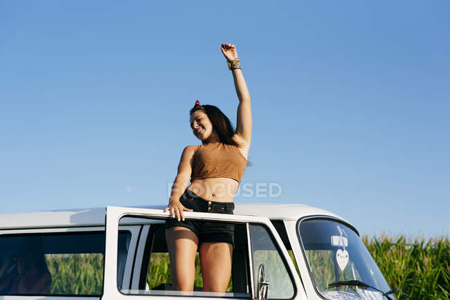 Красивая и счастливая брюнетка, стоящая в фургоне в солнечный день — стоковое фото