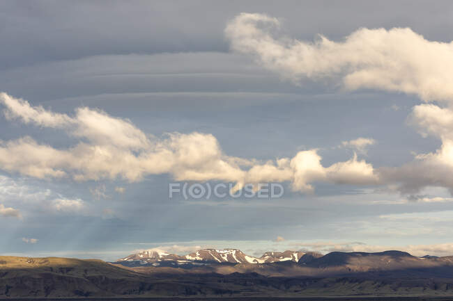 Landscape of hilly area against mountain range covered with snow located against blue sky with clouds in nature of Iceland — Stock Photo
