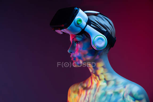 Женский манекен с VR гарнитурой, стоящий под ярким разноцветным освещением на фиолетовом фоне — стоковое фото