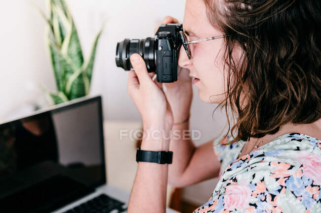Vista lateral da colheita fotógrafa do sexo feminino tirar foto na câmera profissional na sala turva contra computador — Fotografia de Stock