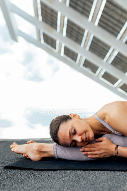 Спокійна жінка з закритими очима, що практикує фронт, розколюється вперед згинається асан на вулиці з сонячною панеллю в місті — стокове фото