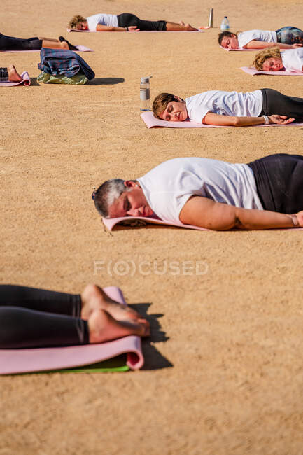 Вид сбоку спокойных женщин в активах, лежащих на ковриках на земле после сеанса йоги в парке при солнечном свете — стоковое фото