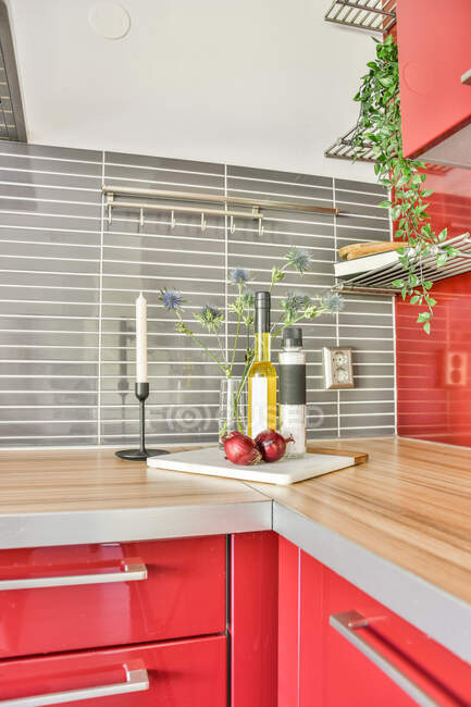 Garrafa de óleo e sal colocada no balcão vermelho com vela e flores na cozinha moderna — Fotografia de Stock