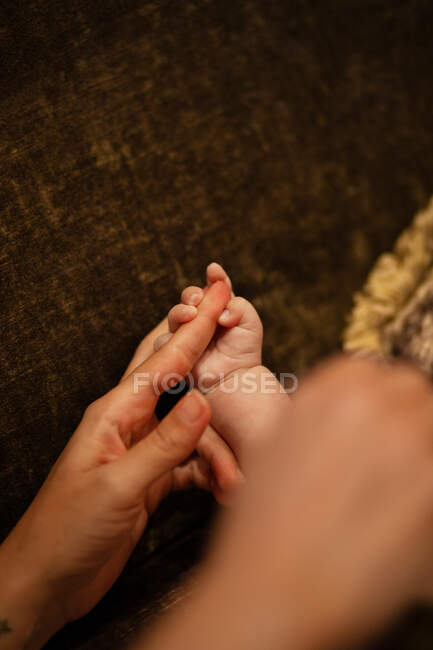 From above of crop unrecognizable baby lying on comfortable couch and holding hand of mother — Stock Photo