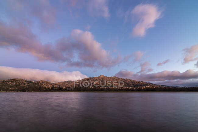 Acqua di mare che scorre contro la riva con ruvida montagna rocciosa contro il colorato cielo blu con nuvole bianche in natura al tramonto — Foto stock