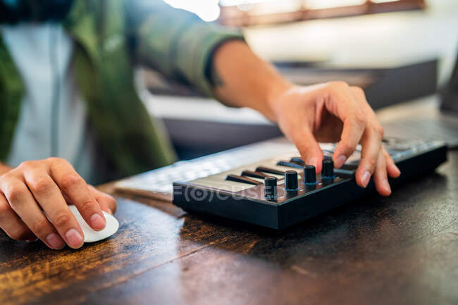 Анонимный музыкант, работающий за компьютером за столом при настройке звука MIDI контроллера в светлом помещении — стоковое фото