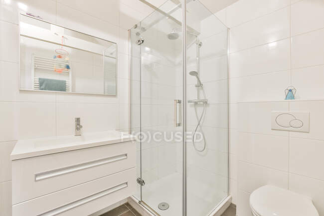 Интерьер современной светлой ванной комнаты с душевой кабиной и туалетом возле раковины под зеркалом в квартире — стоковое фото