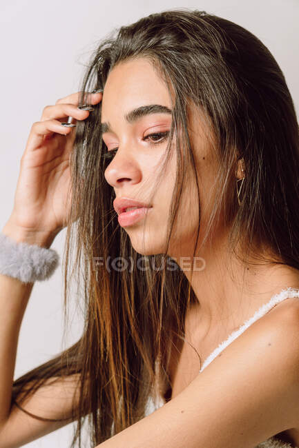 Vista lateral de una joven hispana reflexiva con maquillaje mirando hacia otro lado sobre un fondo claro - foto de stock