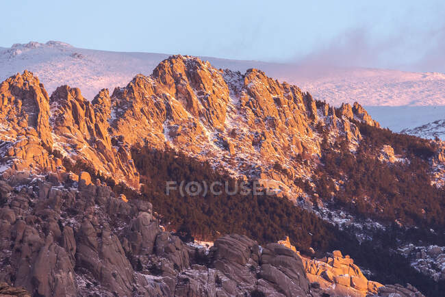 Pietre grezze ricoperte di muschio e cespugli situate sulla cima della montagna innevata nel Parco Nazionale della Sierra de Guadarrama a Madrid, Spagna durante il tramonto — Foto stock