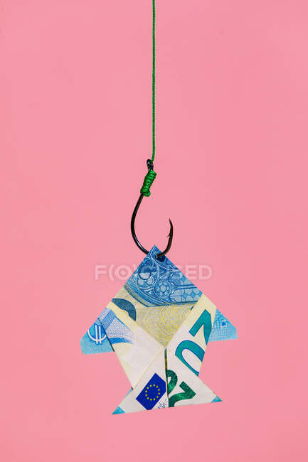 Gancho en línea tirando de origami peces en forma de billete en euros como concepto de riqueza y dinero que gana contra el fondo rosa - foto de stock