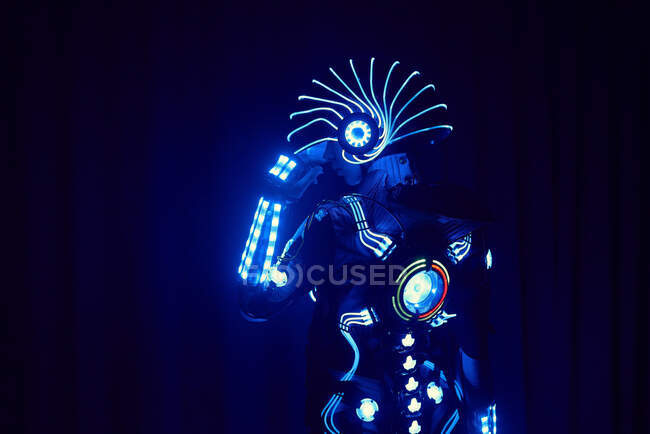 Faceless person in contemporary glowing suit of space cyborg with neon illumination and helmet standing on black background in dark studio — Stock Photo