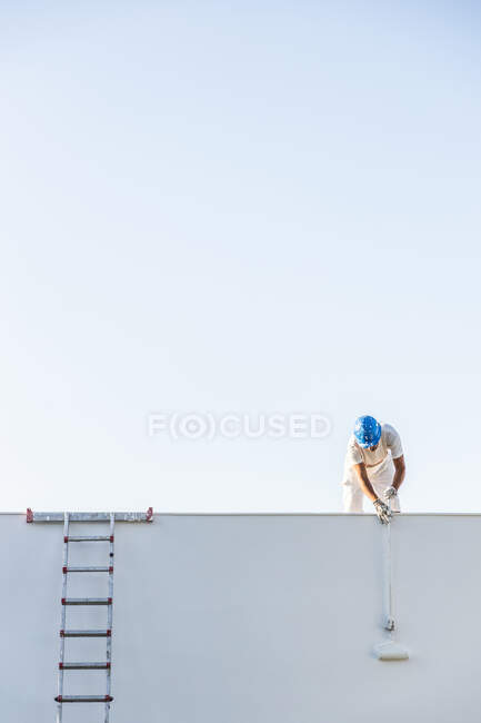 Unbekannter junger Maler bemalt die Fassade einer Wohnung mit einer Walze vom Dach und das Treppenhaus seitlich — Stockfoto