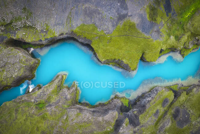 Draufsicht auf den blauen stillen See, der zwischen steilen steinigen Küsten mit grünem Moos bedeckt in der wilden Natur Islands fließt — Stockfoto