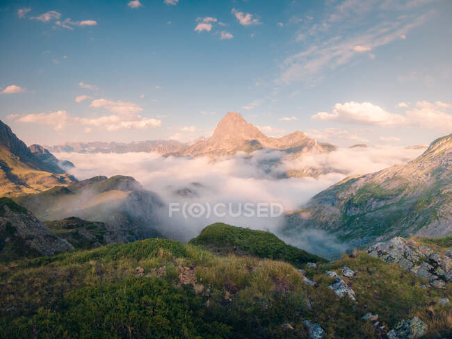 Thick white mist floating near rough rocky mountain ridge against cloudy sky in wild nature of Spain on summer evening — Stock Photo