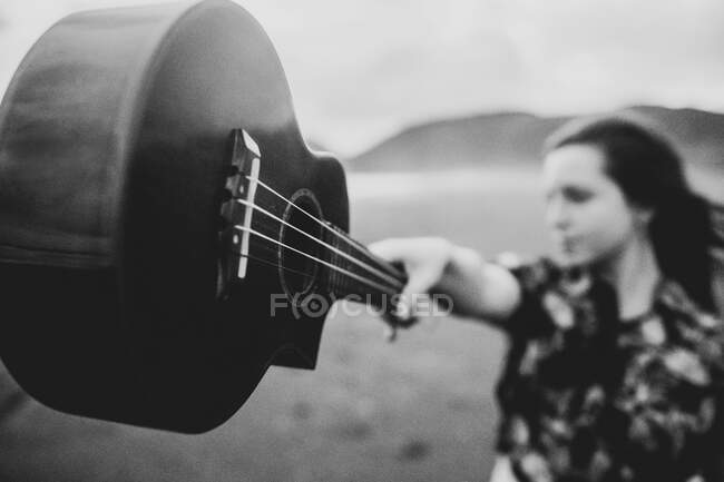 Black and white of calm female in casual clothes standing and reaching out hand with ukulele on sandy beach in daylight — Stock Photo