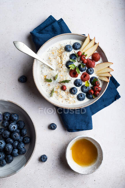 Ciotola vista dall'alto di delizioso porridge condito con mirtilli e lamponi vicino a fette di pera servite sul tavolo durante la colazione — Foto stock