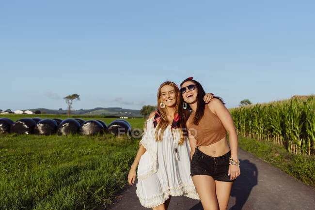 Дві щасливі дівчини, одягнені в літній одяг, розважаються біля вінтажного фургона в сонячний день. — стокове фото