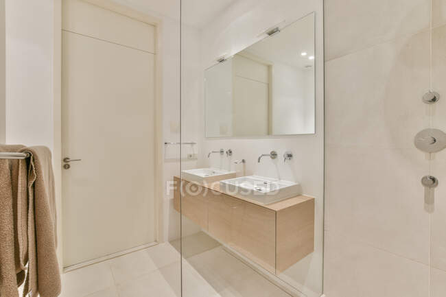 Lavelli bianchi a parete con specchio posizionati vicino alla cabina doccia in vetro in luce ampio bagno con asciugamano e illuminazione luminosa — Foto stock