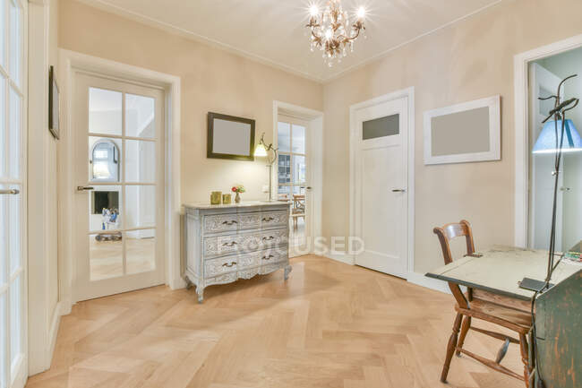 Aged table and cupboard against chair on parquet under shiny chandelier in room with glass doors — Stock Photo
