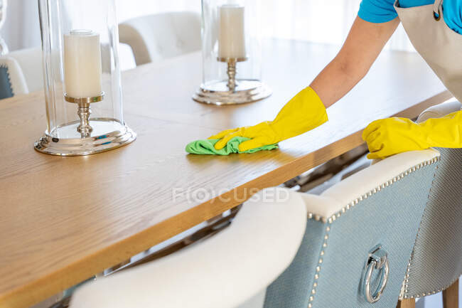 Jeune femme cultivée nettoyant professionnel en uniforme et gants essuyant la poussière de bougeoir élégant placé sur la salle à manger dans une maison spacieuse — Photo de stock