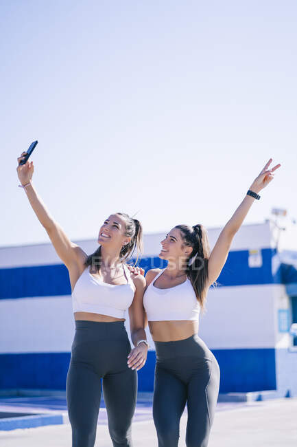 Entzückte sportliche Zwillingsmädchen stehen auf Sportplatz und machen Selfie mit Smartphone — Stockfoto