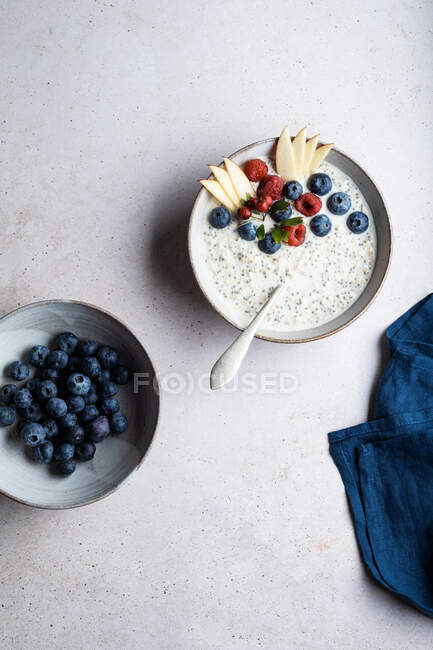 Bol avec vue sur le dessus de délicieux porridge garni de bleuets et de framboises près de tranches de poire servies sur la table pendant le petit déjeuner — Photo de stock
