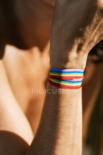Side view of crop unrecognizable person with rainbow ribbon on hand against green plants in summer time — Stock Photo