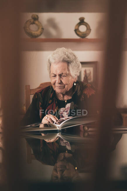 Літня жінка сидить у кріслі і демонструє сімейні фотографії з фотоальбому іншій людині — стокове фото