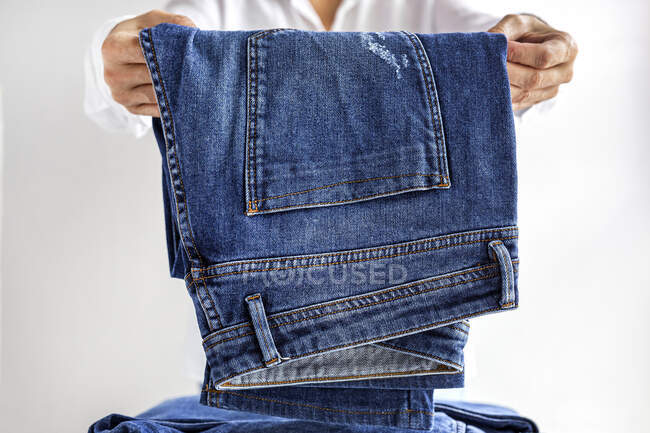 Cortar fêmea irreconhecível em camisa branca empilhando jeans azuis em pilha de roupas após a lavagem — Fotografia de Stock
