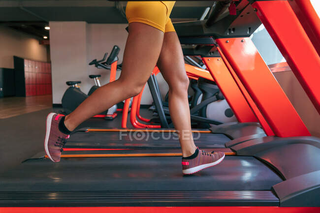Vista lateral da fêmea atlética irreconhecível cortada correndo em esteira rolante no treinamento cardio no ginásio — Fotografia de Stock
