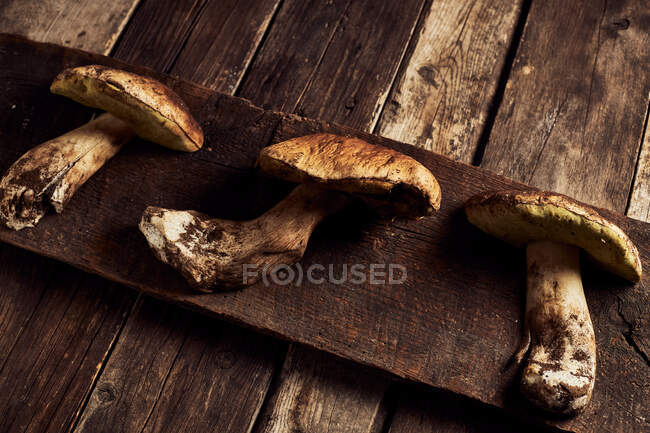 Vista superior do corte cru Boletus edulis cogumelos em tábua de corte de madeira rústica durante o processo de cozimento — Fotografia de Stock