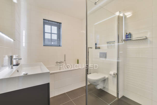 Lavandino e servizi igienici situati vicino alla vasca da bagno dietro la parete di vetro in bagno leggero a casa — Foto stock