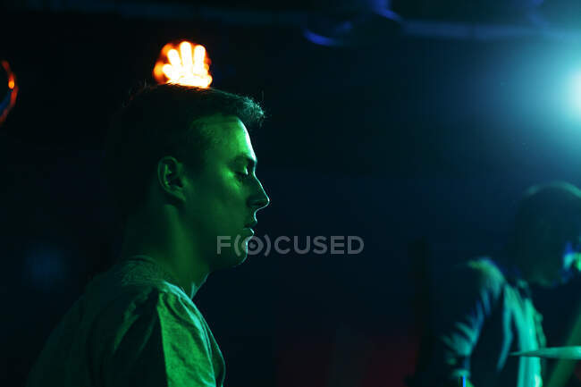 Serious young guys performing music on drums in club with neon green and blue lights — Stock Photo