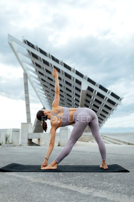 Full body of active woman in sportswear doing yoga asana on mat while standing on street near solar panel in Barcelona — Stock Photo