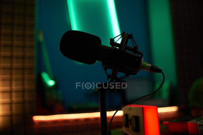 Сучасний мікрофон на тринозі, розміщений на столі в темній студії з неоновим освітленням перед записом подкасту — стокове фото