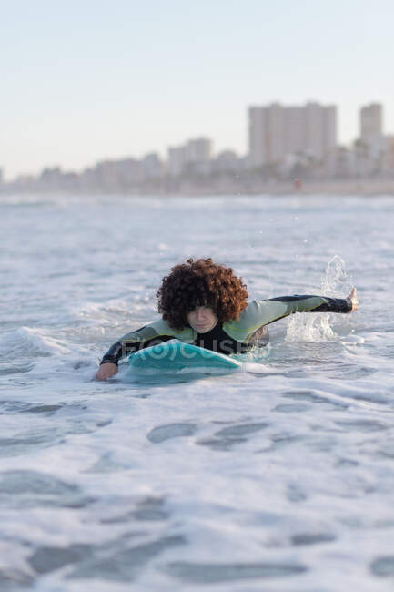 Junge Surferin im Neoprenanzug liegt auf winkendem Meerwasser und genießt den Sommertag — Stockfoto