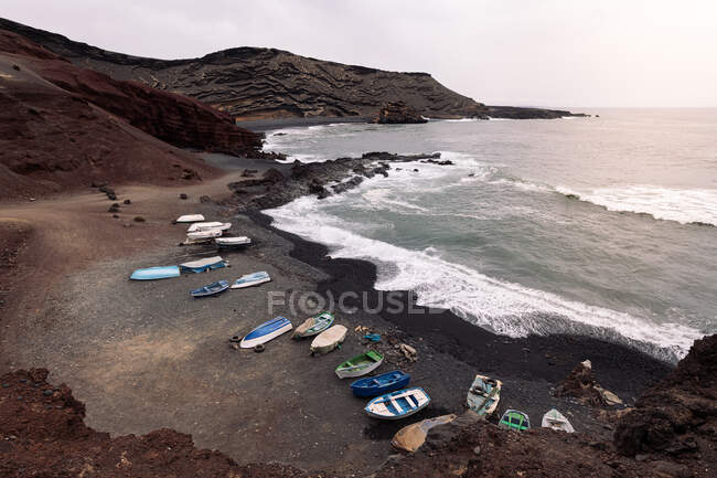 Drone view of boats on Ciclos Beach against foamy ocean and Guincho Volcano in Golfo Yaiza Lanzarote Canary Islands Spain — стокове фото
