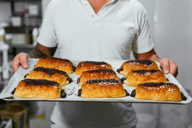 Посадка неузнаваемый мужчина шеф-повар демонстрирует выпечку поднос с вкусными сладкими тортами с шоколадным кремом и посыпать на кухне — стоковое фото