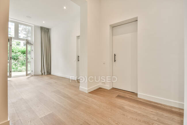 Geräumiger, leerer Raum mit weißen Wänden und Laminatboden in modernem Haus mit Hinterhof im Tageslicht — Stockfoto
