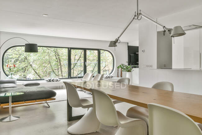 Camera contemporanea e cucina interna con divano e tavolo sotto le lampade contro finestra e libreria in casa — Foto stock