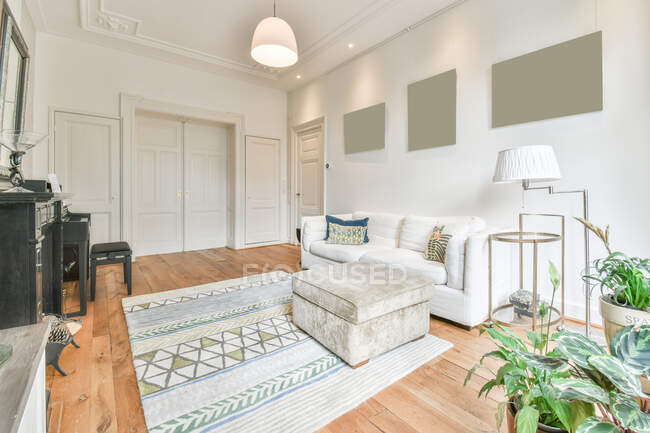 Интерьер гостиной в классическом стиле с удобным диваном рядом с окнами перед фортепиано и камином в светлых просторных апартаментах — стоковое фото