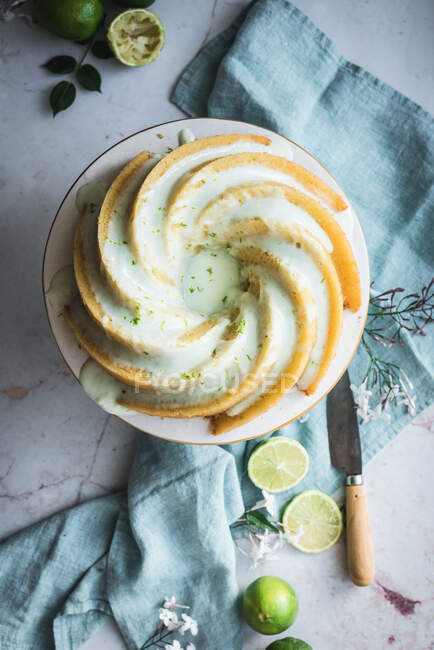 Top view of tasty lime sponge cake served on white plate near flowers and lime slices — Stock Photo