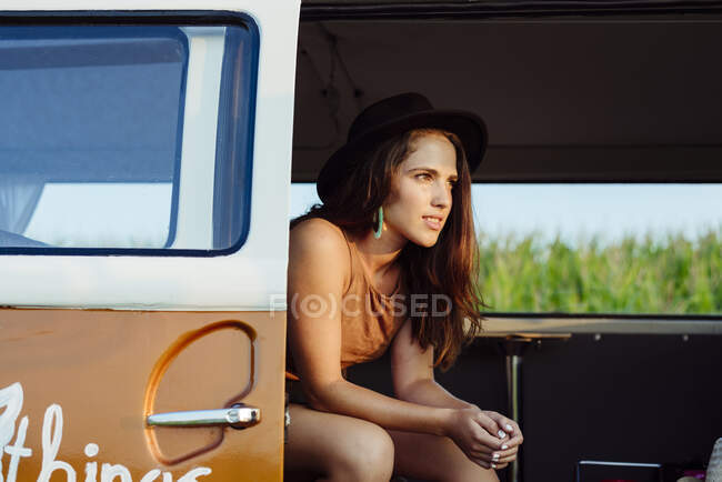 Jolie fille brune avec chapeau à l'intérieur d'un van vintage et assise sur le siège par une journée ensoleillée — Photo de stock