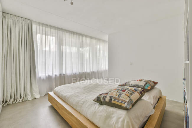 Interior del dormitorio contemporáneo con cama entre tabique de madera y ventana con tul en casa de luz - foto de stock