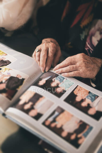 De arriba recorte femenino sentado en sillón y demostrando fotos familiares de álbum de fotos a otra persona - foto de stock
