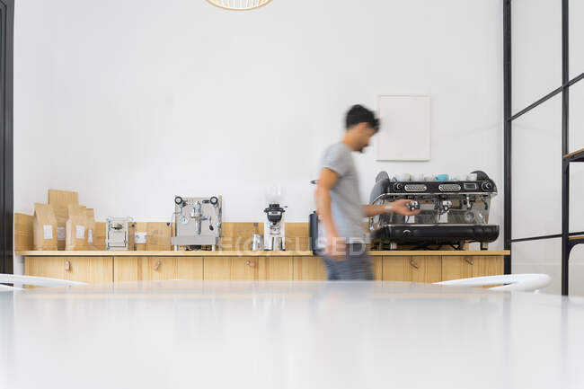 Вид сбоку на безликого бариста, стоящего рядом с современной кофеваркой во время заваривания напитка за стойкой с профессиональным оборудованием в кофейне — стоковое фото